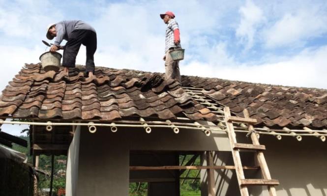 BENAHI ATAP : Dua orang warga ikut membantu membenahi atap pada program bantuan untuk rumah tidak layak huni (Rutilahu). (ILUSTRASI)