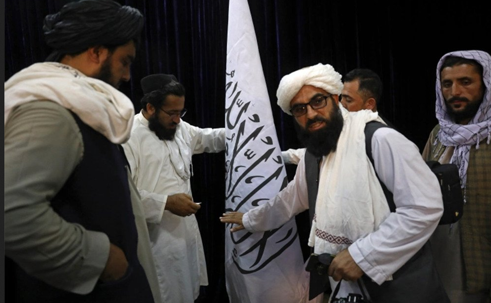 Pejabat Taliban mengatur bendera Taliban, sebelum konferensi pers oleh juru bicara Zabihullah Mujahid di Pusat Informasi Media Pemerintah, Kabul, Afghanistan, Selasa (17/8). Foto: Rahmat Gul/AP Photo