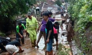 Warga desa di Kecamatan Sukawening tengah membersihkan jalan setelah diterjang banjir bandang