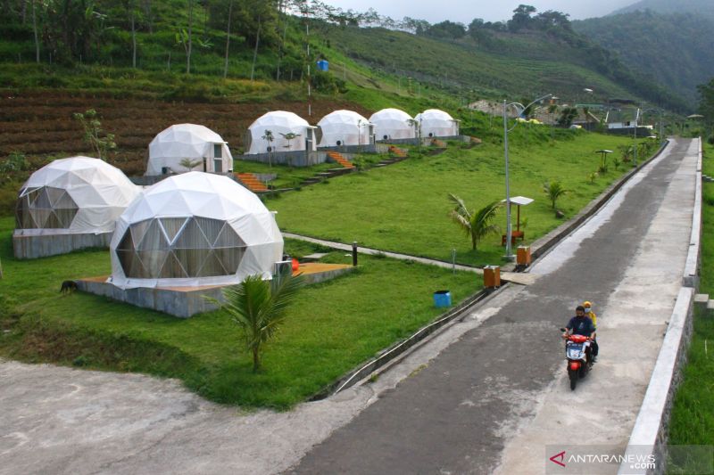 Wisatawan melintas di samping bangunan penginapan tahan gempa di Lembah Indah Resort, Malang, Jawa Timur, Selasa (8/6/2021). Destinasi wisata di lembah gunung Kawi tersebut diminati wisatawan karena aman dari gempa serta memiliki area perkemahan dengan lahan pertanian organik dan rumah kaca sehingga bisa dimanfaatkan sebagai wahana wisata edukasi. ANTARA FOTO/Ari Bowo Sucipto/nz (ARI BOWO SUCIPTO/ARI BOWO SUCIPTO)