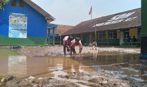 Dua anak tengah bermain lumpur di lapangan upacara SDN 07 Rancaekek pasca diterjang banjir. (Jabar Ekspres)
