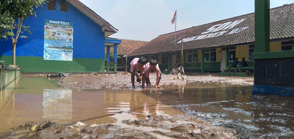 Dua anak tengah bermain lumpur di lapangan upacara SDN 07 Rancaekek pasca diterjang banjir. (Jabar Ekspres)
