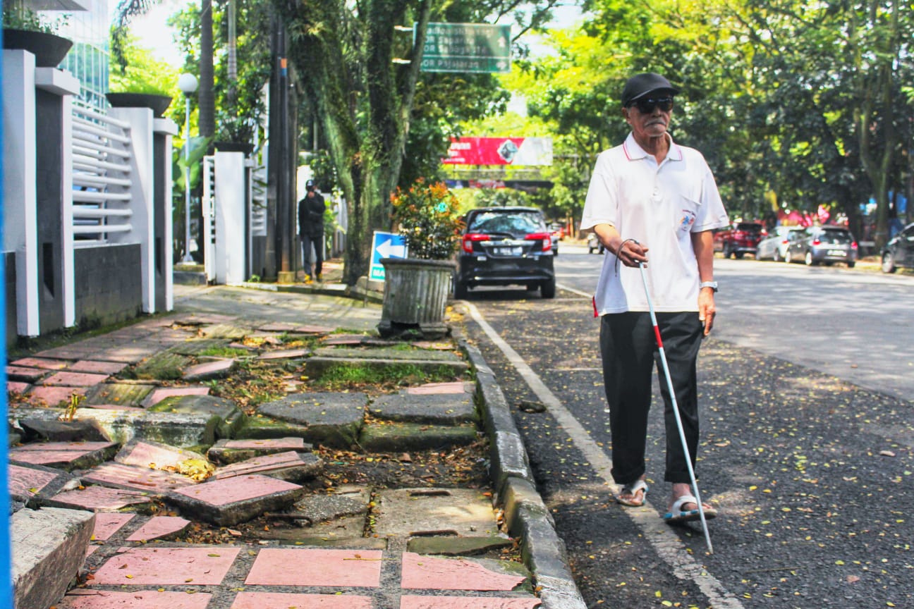 TUNANETRA: Seorang penyandang disabilitas tunanetra saat menggunakan bahu jalan, lantaran trotoar rusak dan membahayakan. (Deni/Jabar Ekspres)