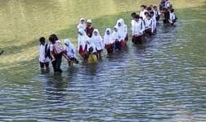 Puluhan anak SD yang tampak sedang menyebrangi sungai saat menuju kesekolahnya.