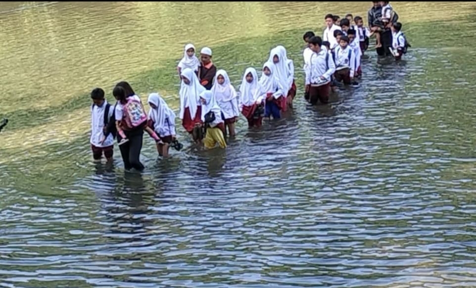 Puluhan anak SD yang tampak sedang menyebrangi sungai saat menuju kesekolahnya.