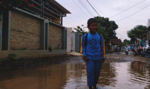 LEWATI KUBANGAN: Seorang anak melintasi jalan berlubang di Desa Mekarmukti Kecamatan Cihampelas, KBB. (Akmal Firamsnyah/Jabar Ekspres)