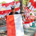 Rehan alias Ubek (33) sedang memegang bendera Merah Putih di lapak tempatnya berjualan di Sumedang, Jum'at 4 Agustus 2023.