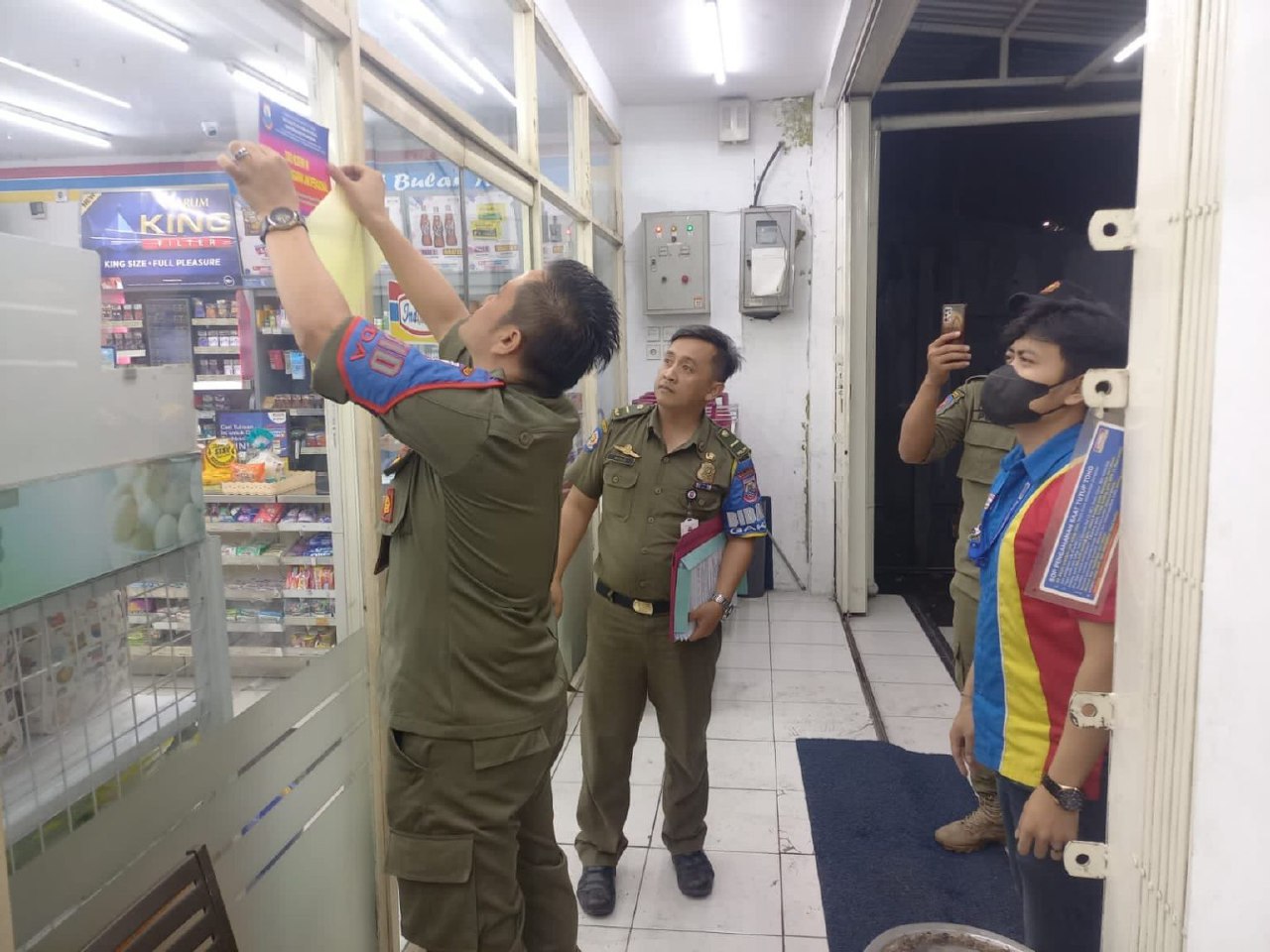 Kepala Bidang Gakda Satpo PP dan Damkar Kota Cimahi Ranto Sitanggang memasang stiker di bagian depan toko modern yang melanggar jam operasional.