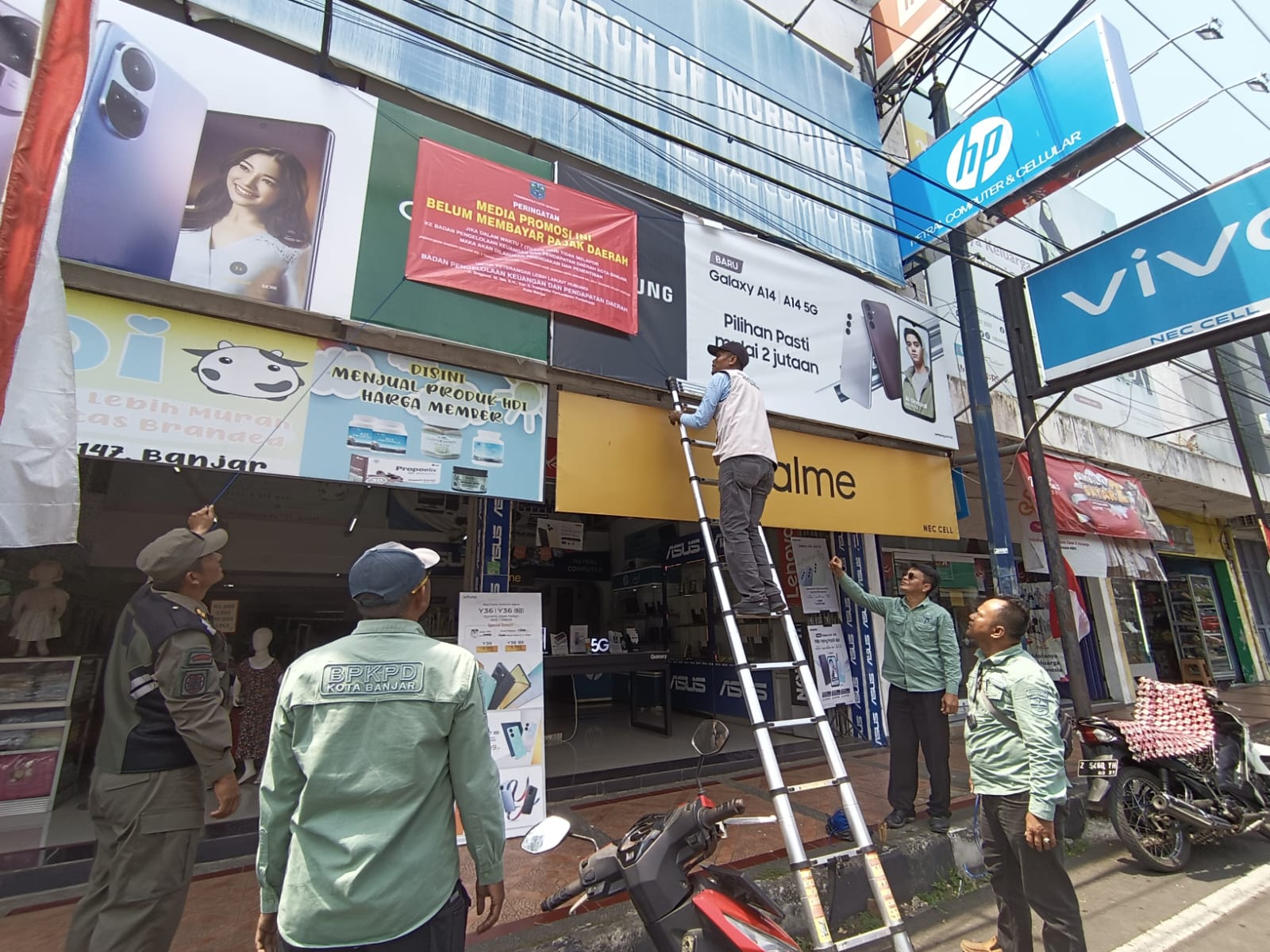 Petugas dari Bidang Pendapatan Kota Banjar dan PPNS Satpol PP Kota Banjar memasang media peringatan di papan reklame salah satu brand handphone ternama yang menunggak pajak di salah satu konter di Kota Banjar, Selasa (19/8).