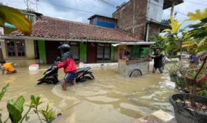 Seorang pengendara motor dan pedagang yang melintasi banjir di Kampung Bojong Asih, Dayeuhkolot, Kabupaten Bandung, Jumat (1/12/2023). Foto Agi Jabar Ekspres