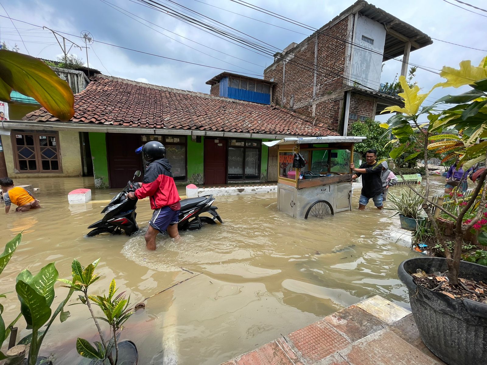 Seorang pengendara motor dan pedagang yang melintasi banjir di Kampung Bojong Asih, Dayeuhkolot, Kabupaten Bandung, Jumat (1/12/2023). Foto Agi Jabar Ekspres