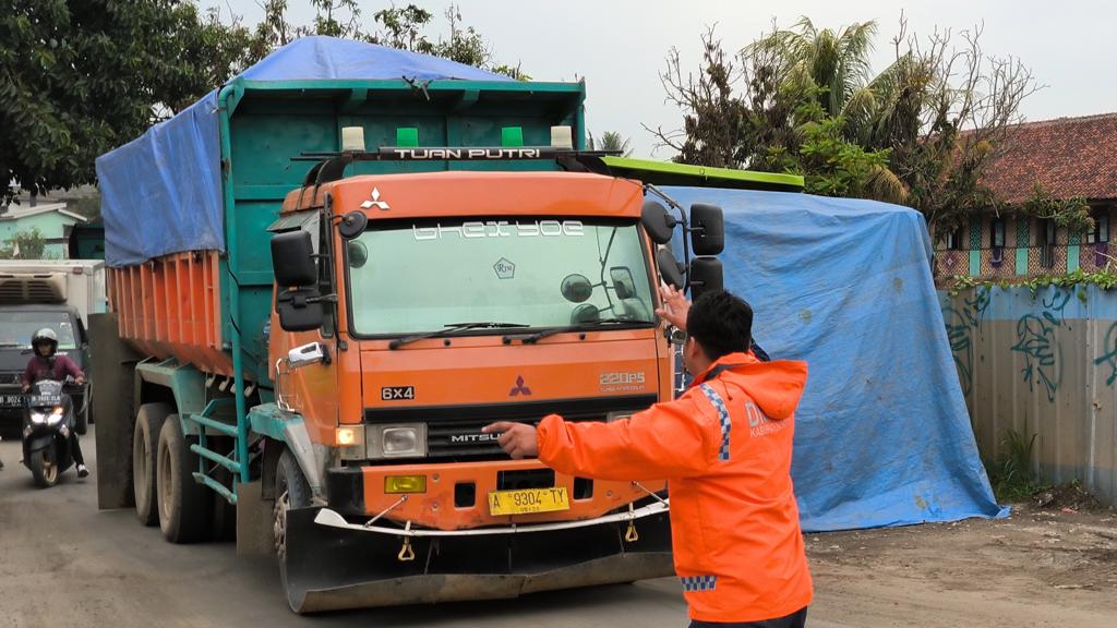 Petugas Dishub Kabupaten Bogor mengatur lalu lintas di Jalan Parung Panjang yang masih dilalui oleh truk diluar jam operasionalnya.