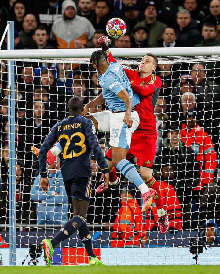 Kiper Real Madrid, Andriy Lunin (merah), saat menghalau bola di udara melawan Manchester City, Kamis (18/4).