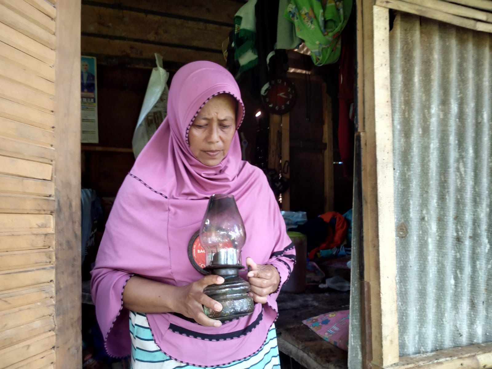 Herlina, istri Engkus berdiri memegang cempor di depan gubuk reyot di pinggiran hutan Kota Banjar, baru-baru ini. (Cecep Herdi/Jabar Ekspres)