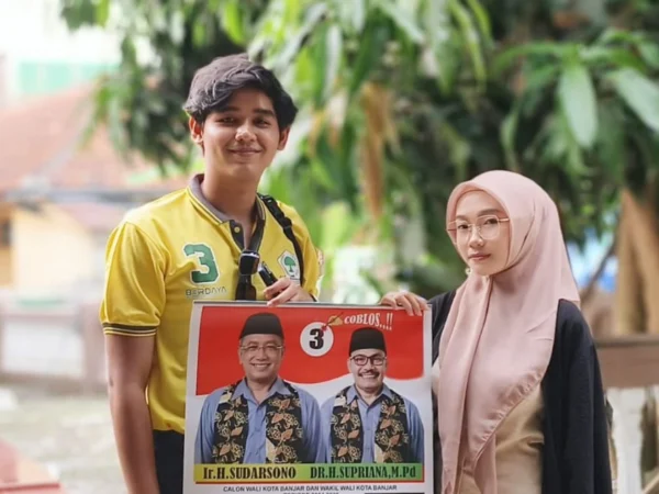 Dua muda-mudi memegang gambar berisikan pasangan calon Walo Kota dan Wakil Walikota Banjar nomor urut 3, Sudarsono dan Supriana. Paslon ini menjanjikan Tunjangan Daerah (Tunda) ASN Guru diberikan lagi. (Foto:Istimewa)