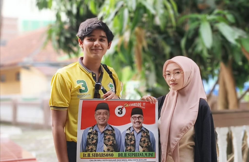 Dua muda-mudi memegang gambar berisikan pasangan calon Walo Kota dan Wakil Walikota Banjar nomor urut 3, Sudarsono dan Supriana. Paslon ini menjanjikan Tunjangan Daerah (Tunda) ASN Guru diberikan lagi. (Foto:Istimewa)