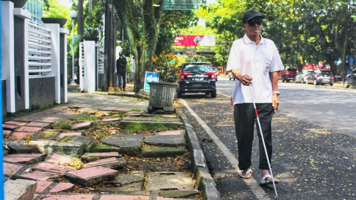 TUNANETRA: Seorang penyandang disabilitas tunanetra saat menggunakan bahu jalan, lantaran trotoar rusak dan membahayakan di Kota Bandung. (Ilustrasi/Jabar Ekspres)