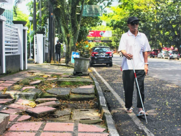 TUNANETRA: Seorang penyandang disabilitas tunanetra saat menggunakan bahu jalan, lantaran trotoar rusak dan membahayakan di Kota Bandung. (Ilustrasi/Jabar Ekspres)