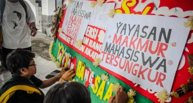 Ist. Sejumlah mahasiswa Universitas Bandung menempelkan poster tuntutan kepada pihak kampus di sebuah karangan bunga di Kampus Utama Universitas Bandung, Jalan Muararajeun, Kota Bandung, Senin (6/1). Foto: Dimas Rachmatsyah / Jabar Ekspres