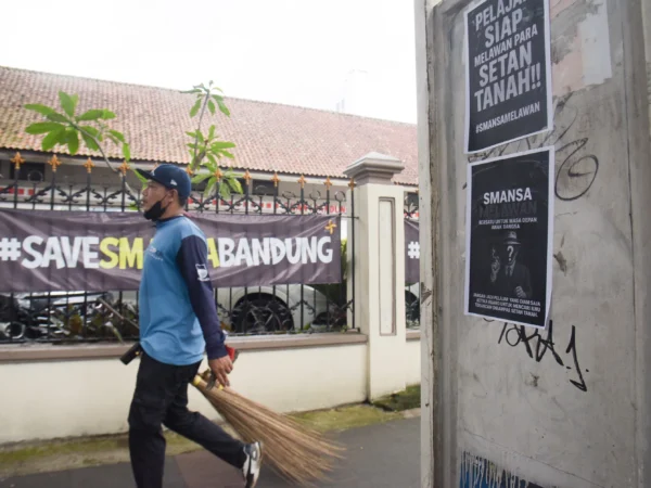 Petugas kebersihan berjalan di samping poster perlawanan di depan SMA Negeri 1, Kota Bandung, Senin (21/4). Foto: Dimas Rachmatsyah / Jabar Ekspres
